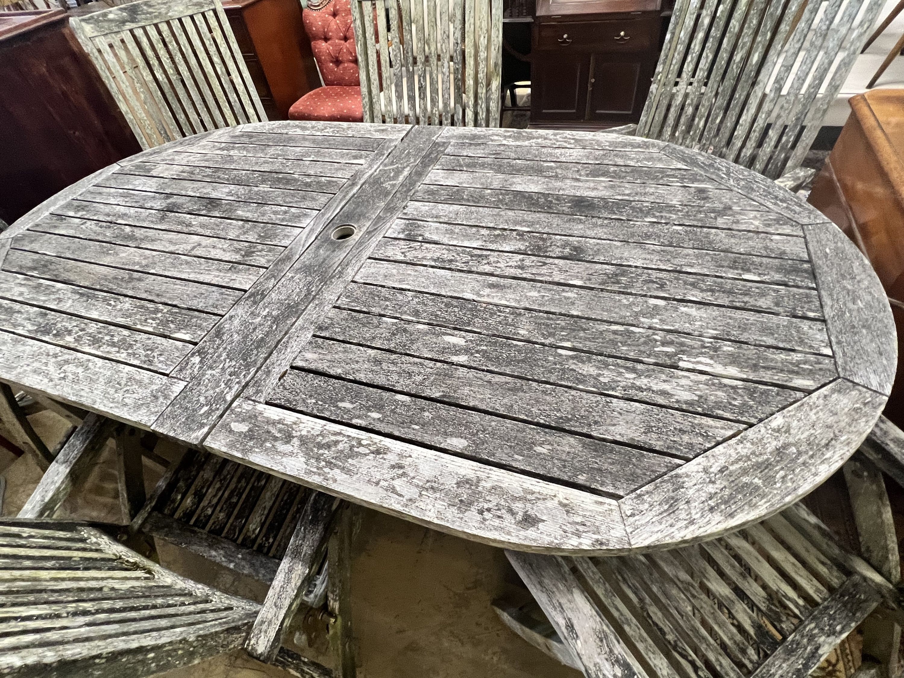 A weathered teak oval extending garden table, extended 250cm width 109cm height 73cm, and six folding garden elbow chairs